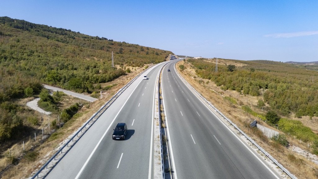 Панорамен изглед към АМ „Хемус“ с автомобили, движещи се сред зелени хълмове и открита пътна отсечка.