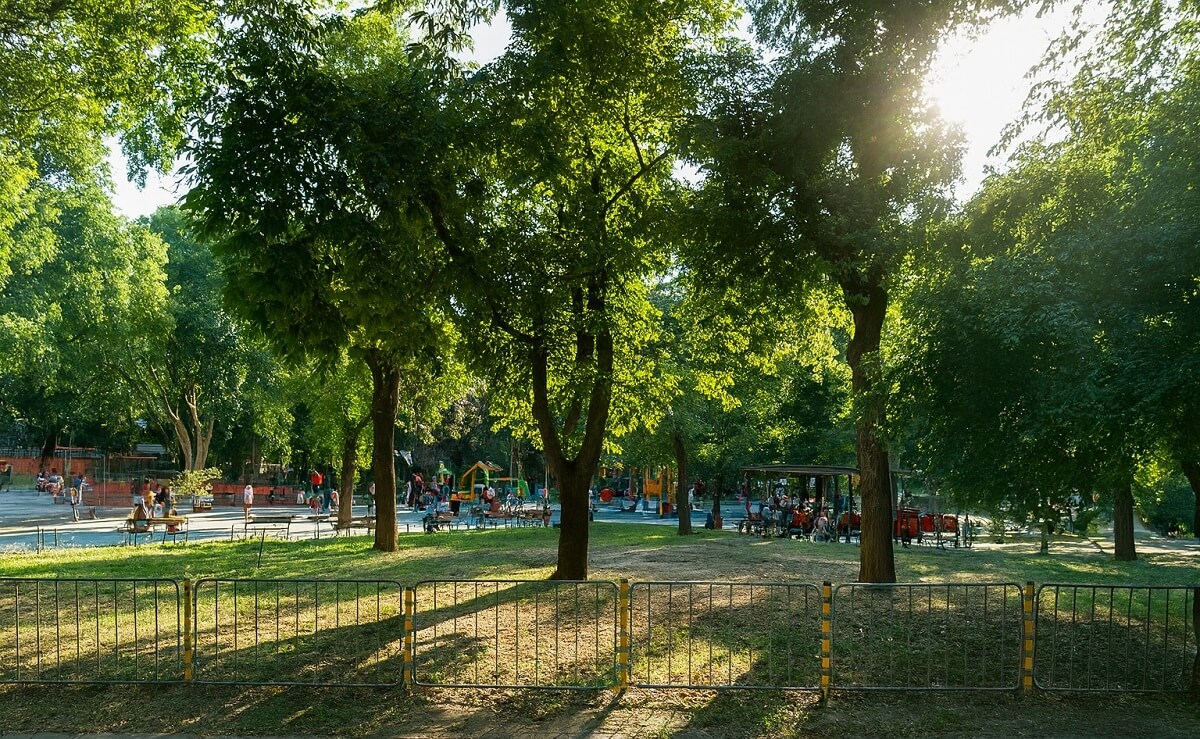 Детска площадка и алеи в градинка във Варна, с дървета и хора, заснети в слънчев следобед