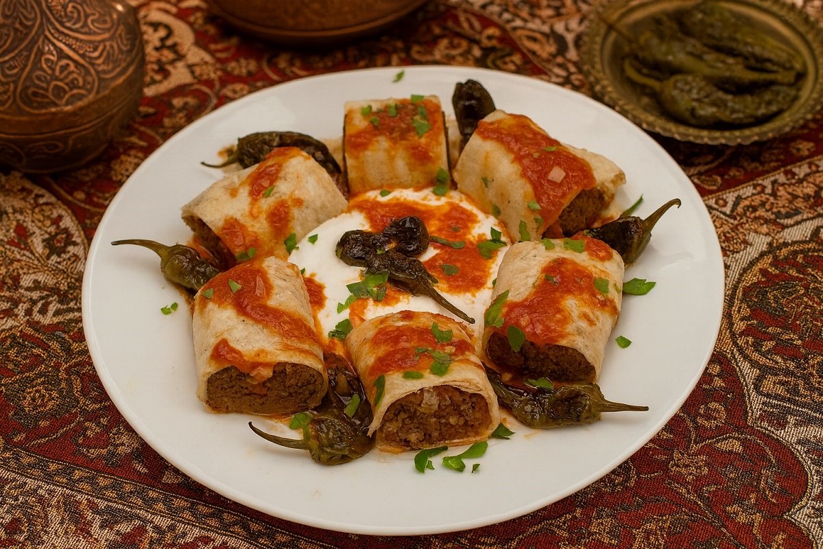 „Домашен бейти кебап, поднесен в ориенталски стил – нарязани рулца от месо, увити в тънка питка, с доматен сос, чесново кисело мляко и печени зелени чушки, сервирани върху богато украсена ориенталска покривка.“