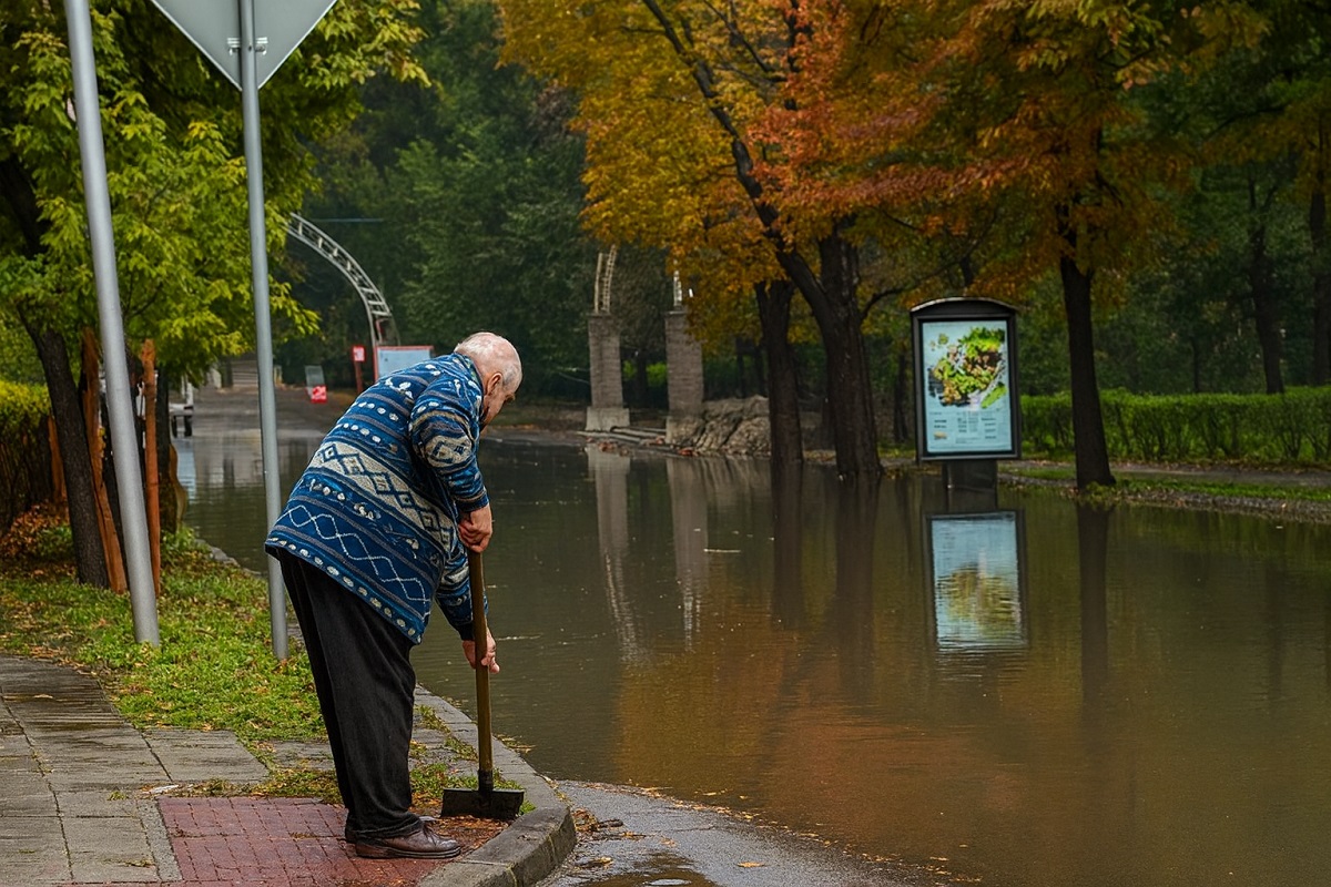 Възрастен мъж почиства шахта на наводнена улица през есента, за да може водата да се оттече.