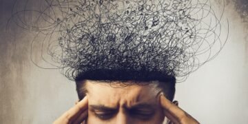 Мъж държи главата си с пръсти в знак на напрежение, а над нея се издигат хаотични линии, символизиращи тревожни мисли и стрес.