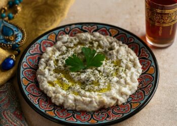 „Ориентална салата от печен патладжан с кисело мляко, чесън и билки, поднесена в декоративна шарена чиния с поръсено зехтиново масло, до нея стъклена чаша с чай и златиста ориенталска кърпа.“