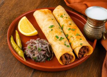 Традиционен турски тантуни, поднесен в тънък лаваш с парченца месо, люта туршия и резени лимон, до чаша айрян в меден съд – сервирано в типичен турски стил върху дървена маса.