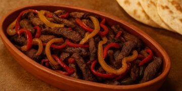 Ориенталско ястие с запържено телешко месо и цветни чушки, поднесено в глинен съд, със свежо изпечени тортили на заден план.