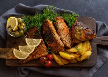 „Печен пълнен шаран за Никулден, поднесен с лимон, копър и картофи върху дървена дъска“