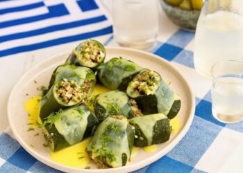 Пълнени тиквички в гръцки стил, поднесени с авголемоно сос върху синьо-бяла покривка, с узо и средиземноморски акценти.