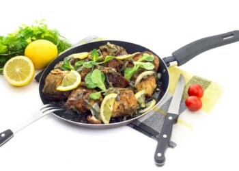 Паламуд на тиган с лимон и зелени подправки, поднесен в черен съд върху светъл фон