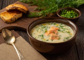 Рибена чорба по варненски, сервирана в тъмна купа с копър и препечени филийки върху дървена дъска