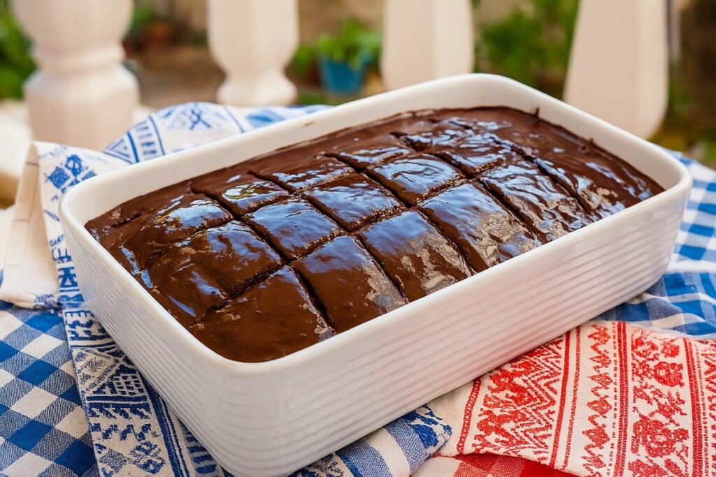 Апетитен гръцки шоколадов сладкиш Sokolatopita, поднесен в бяла тава, с блестящ шоколадов топинг, заснет в типична гръцка обстановка на дървена маса.