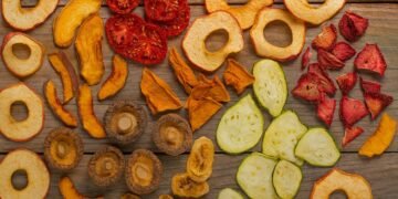 Асортимент от домашно сушени плодове и зеленчуци – ябълки, домати, тиквички, гъби, банани, кайсии и ягоди, подредени върху дървена повърхнос