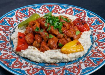 Ароматно ястие Али Назик кебап – нежни късчета агнешко в доматен сос върху крем от патладжан и кисело мляко, поднесени в чиния с турски орнаменти и печени чушки.