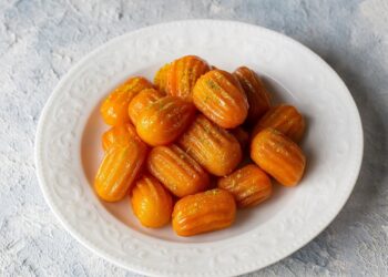 Чиния със златисти, хрупкави и сиропирани тулумбички върху светъл фон.