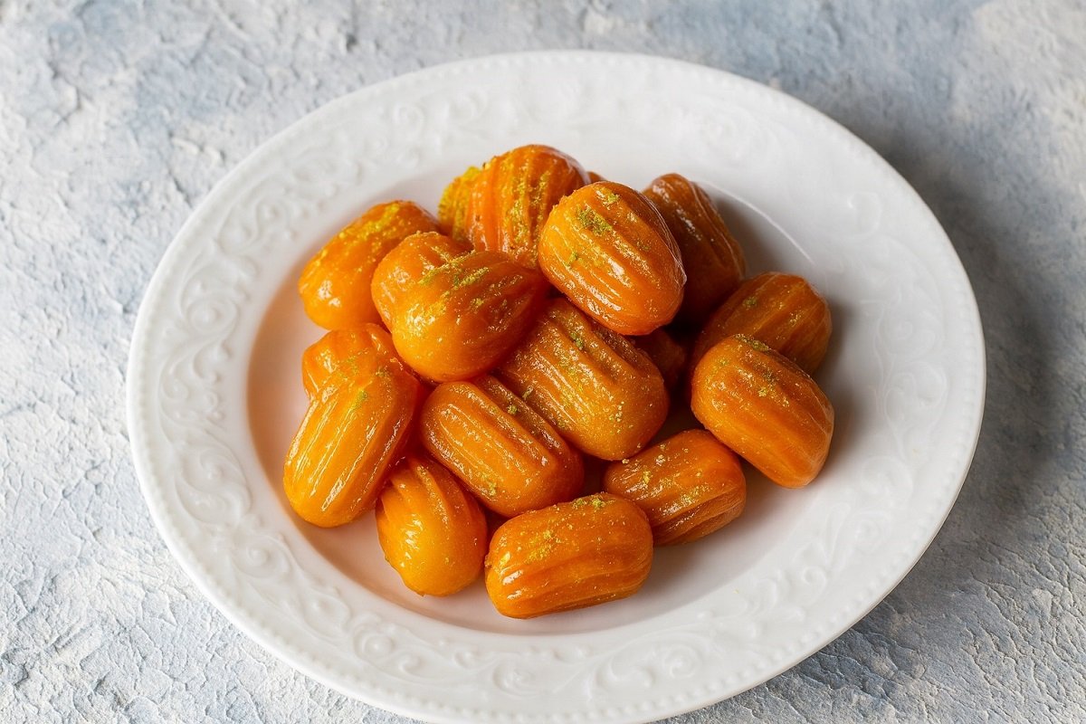 Чиния със златисти, хрупкави и сиропирани тулумбички върху светъл фон.