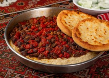 Традиционна турска тава с месо и зеленчуци, поднесена на ориенталска маса с хляб и подправки — ароматно домашно ястие, вдъхновено от турската кухня.