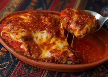 Апетитни печени кюфтета в глинен съд с разтопен кашкавал и доматен сос върху ориентален фон – традиционно ястие, заснето в примамлив детайл