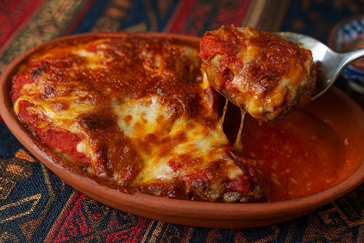 Апетитни печени кюфтета в глинен съд с разтопен кашкавал и доматен сос върху ориентален фон – традиционно ястие, заснето в примамлив детайл