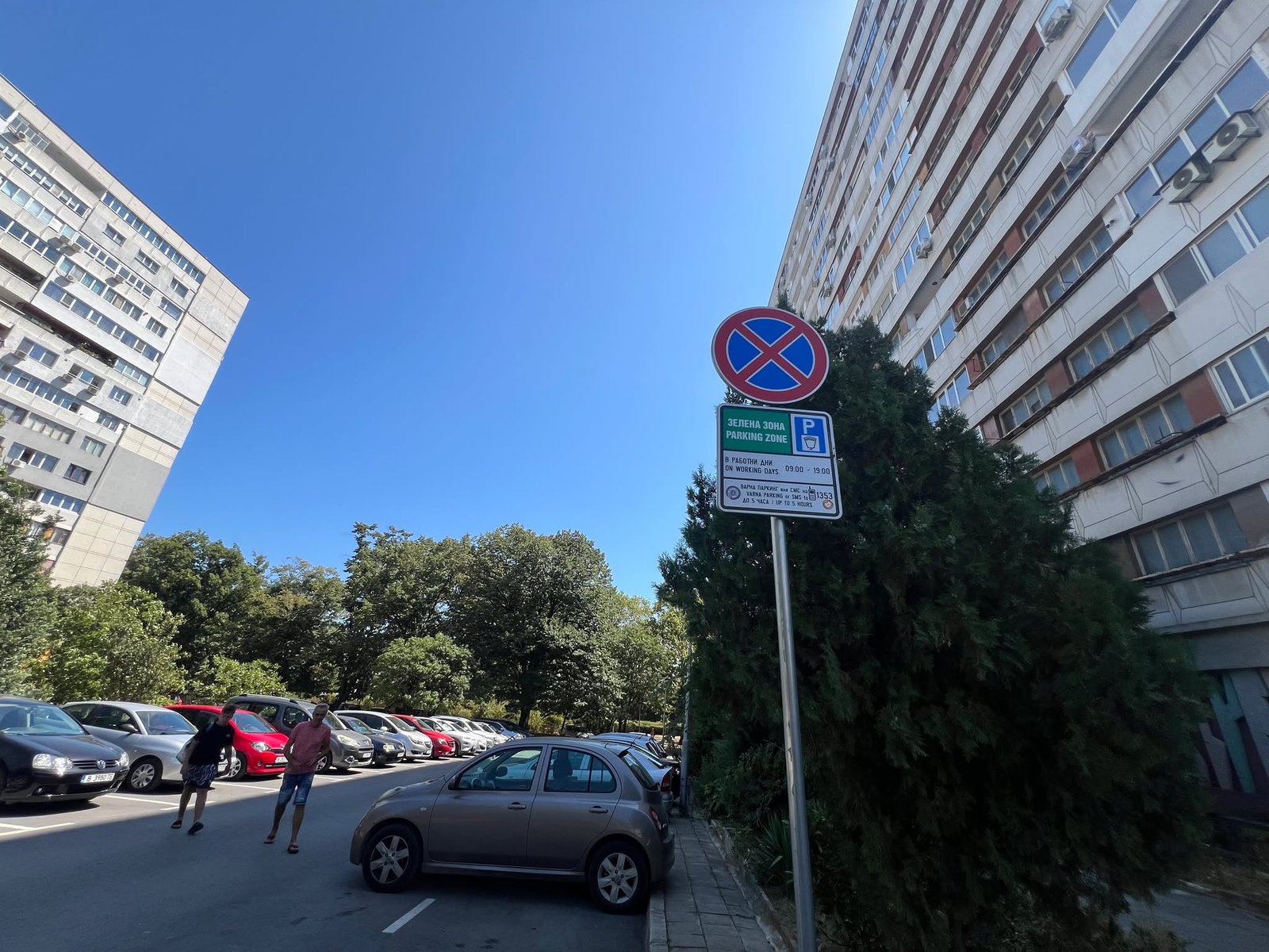 Пътен знак за „Зелена зона“ във Варна, разположен между високи жилищни блокове и паркирани автомобили в слънчев летен ден