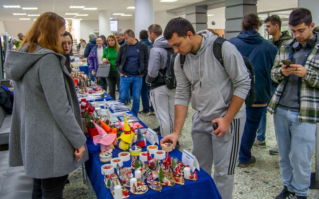 Коледен благотворителен базар в ТУ – Варна с щандове, посетители и предмети за търг в подкрепа на студент със зрително увреждане.