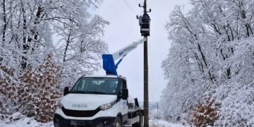 Електротехник отстранява авария по електропровод върху стълб с автовишка и сервизен камион на заснежен път през зимата