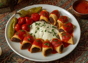 Бейти кебап, поднесен в ориенталски стил – златисти рулца с месо, поляти с доматен сос и кисело-млечен сос, гарнирани с печени чушки и чери домати върху декоративна ориенталска покривка.