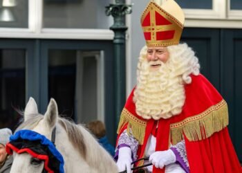 Празничен образ на Свети Николай / Синтерклаас – мъж в червена мантия и златна митра, яздещ бял кон по време на традиционно шествие.