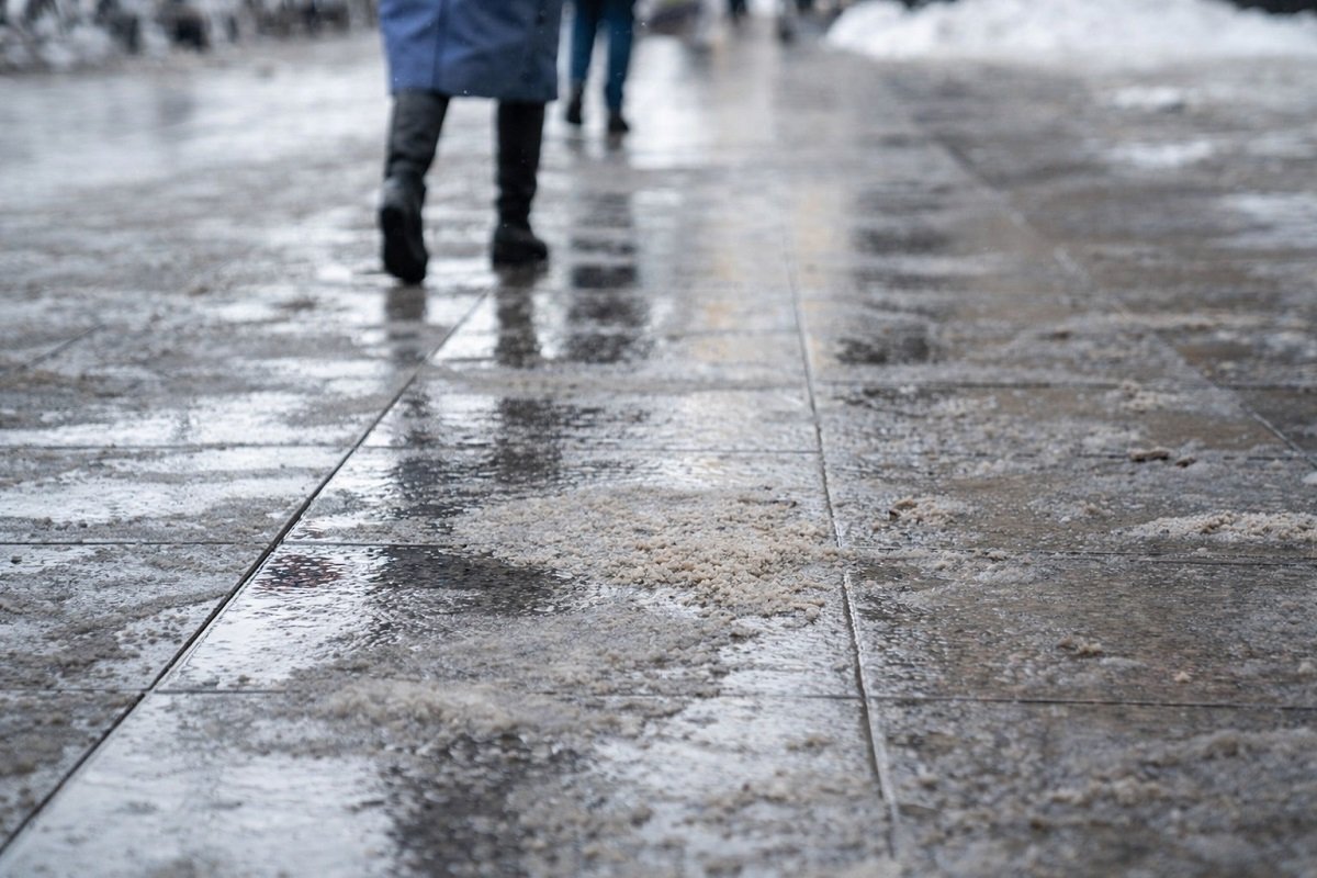 Заледен тротоар в градска среда с пешеходци в зимни условия, хлъзгава настилка и риск от подхлъзване