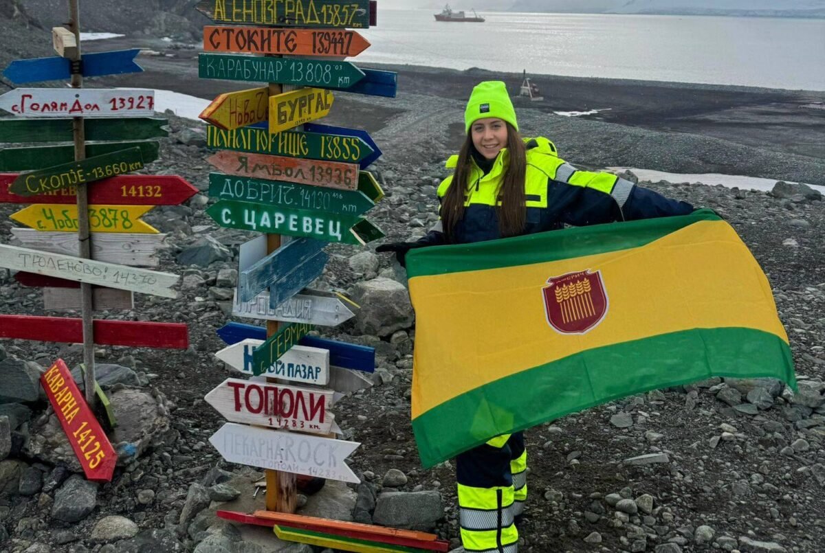 Млада българска военнослужеща развява знамето на град Добрич на остров Ливингстън в Антарктида, на фона на леден пейзаж