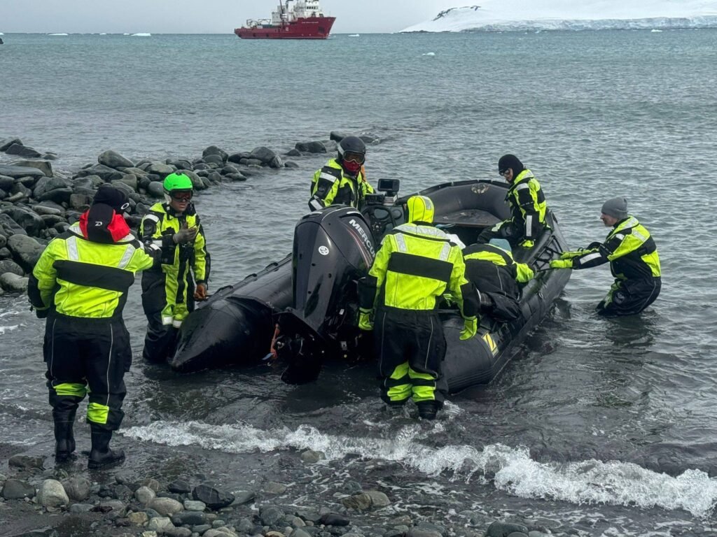 Български полярници с лодка „Зодиак“ по време на теренна работа в Антарктика, облечени в защитни костюми за потапяне.