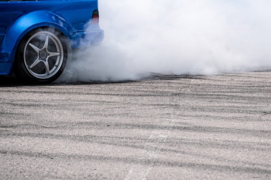Син автомобил дрифтира на асфалт, задното колело се върти и вдига гъст дим
