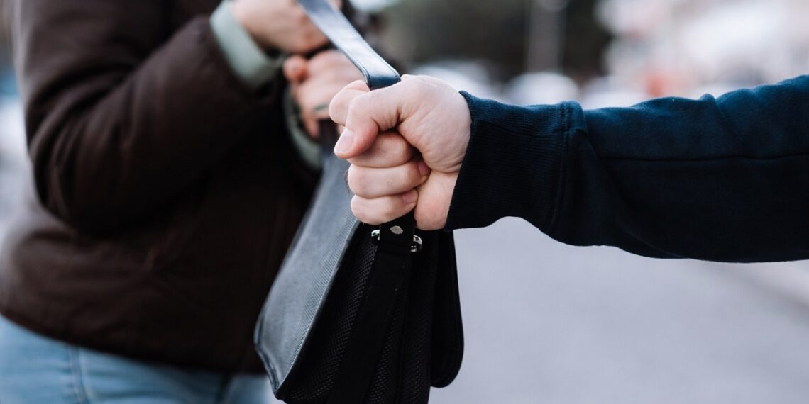 Грабеж на дамска чанта – мъж издърпва чанта от ръцете на жена на градска улица, близък план.