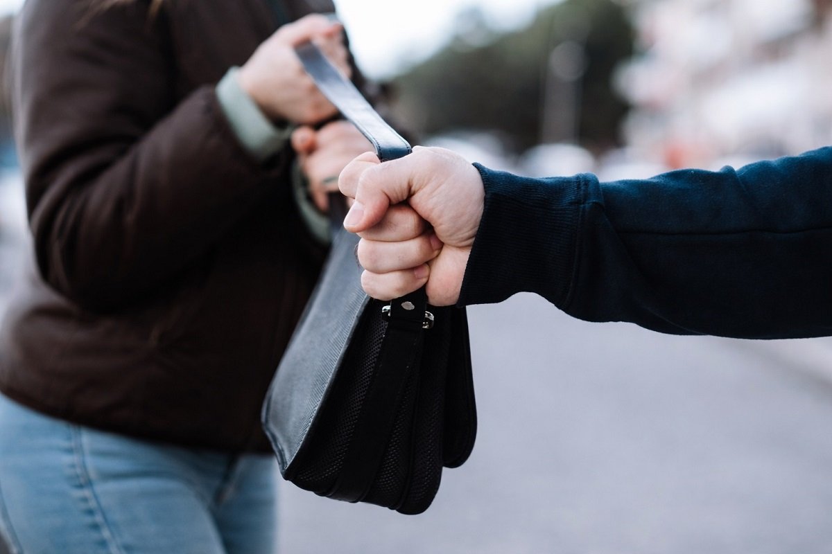 Грабеж на дамска чанта – мъж издърпва чанта от ръцете на жена на градска улица, близък план.