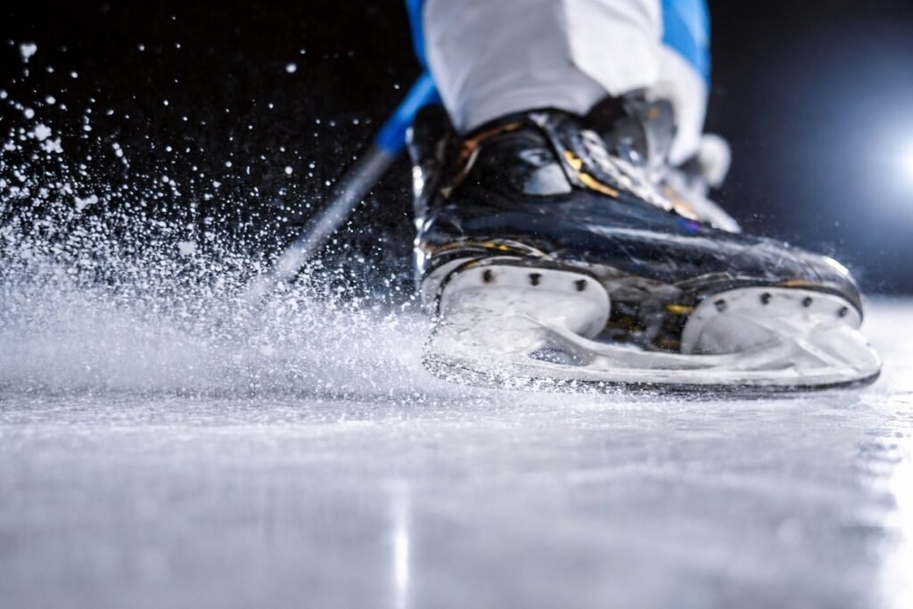 Детайлен кадър на хокейна кънка, която реже леда и разпръсква ледени частици по време на движение в ледена пързалка.
