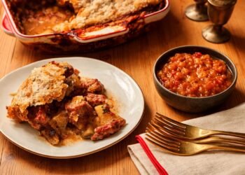 Домашен месен пай със златиста хрупкава коричка, поднесен върху дървена маса с порция, сос и прибори – апетитна хоризонтална кулинарна сцена без надписи