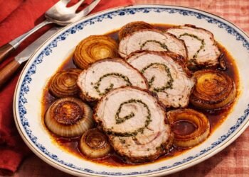 Свинско бонфиле с прошуто и билки, нарязано на резени и сервирано с печен лук