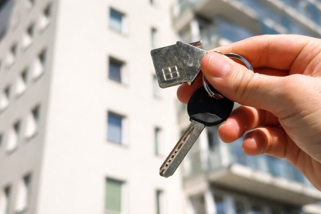Ръка държи ключ за нов апартамент пред модерна жилищна сграда