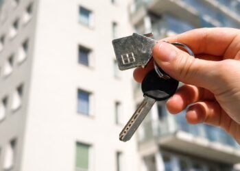 Ръка държи ключ за нов апартамент пред модерна жилищна сграда