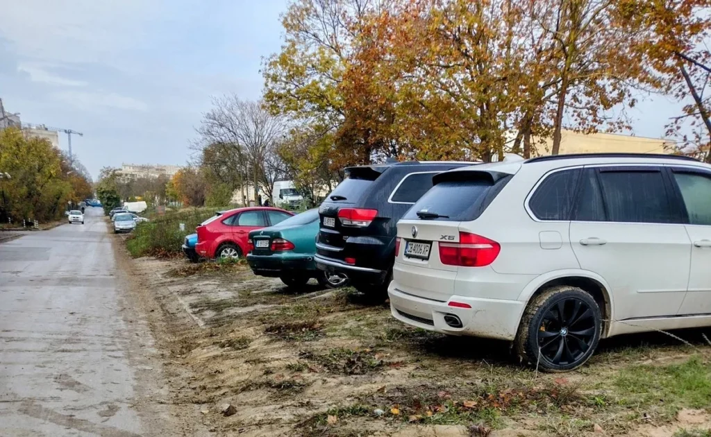 Автомобили паркирани върху кал и зелени площи във Варна до жилищни сгради