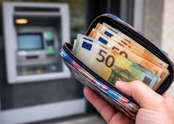 Ръка държи цветно портмоне с евробанкноти пред банкомат на открито във Варна